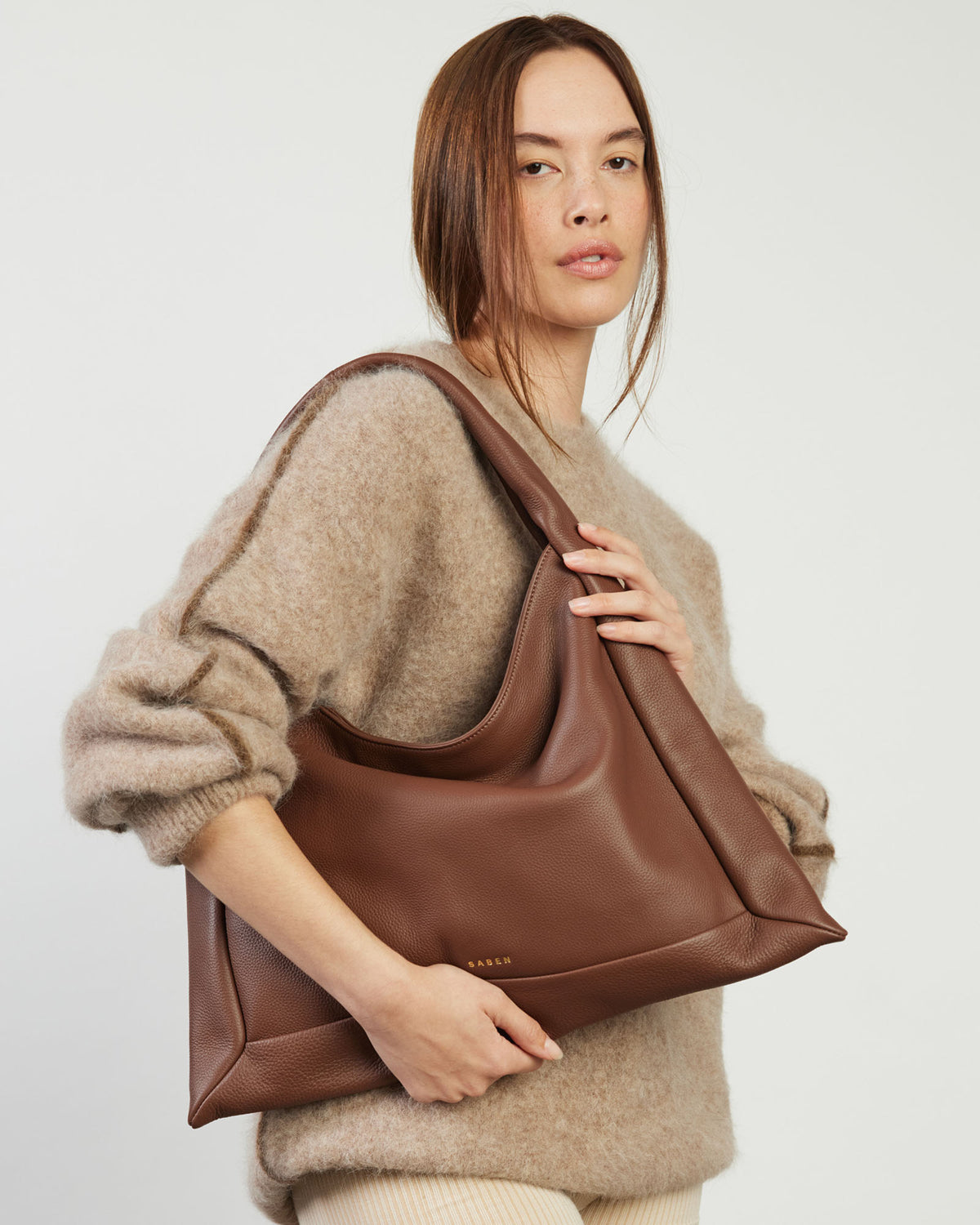Woman holding a brown leather handbag against a plain background